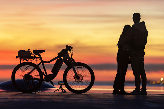 Young couple hugging and looking at the sunset standing by a bicycle