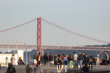 A crowd of tourists on the embankment against the backdrop of the famous 25 de Abril Bridge