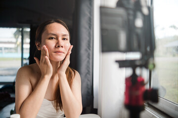Fototapeta na wymiar beauty at home concept, Asian female influencer Applying cream to the face, in front of the camera.