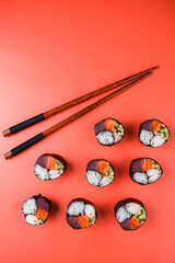 Maki sushi rolls with tuna, salmon, shrimp, cucumber, rice and chopsticks on red background.