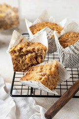 Oatmeal muffins in white paper cups on cooling rack with knife on white textured background close up