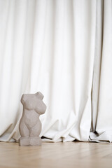 a small antique statues of nude woman body on pedestal, made of gray clay on a beige fabric background. the concept of femininity, freedom, place for an inscription, postcard,femiists.selective focus