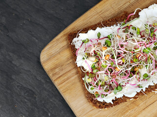 Obraz na płótnie Canvas top view of whole grain bread with cream cheese and sprouts mix on wooden cutting board, healthy breakfast with micro greens
