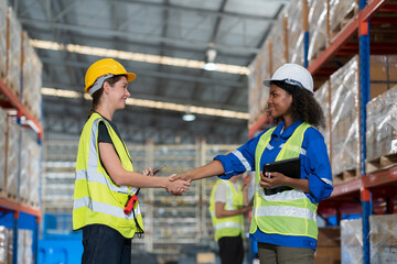 Two female warehouse workers shaking hands together in the storage warehouse, feeling happy and smiling, completed finished job and teamwork successful concept