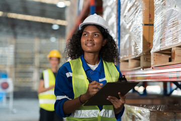 Female warehouse worker wearing hard hat and uniform checks stock and inventory in the retail warehouse