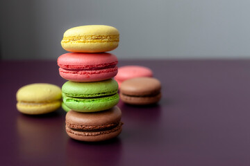 Pile of multi color macaroon or macaron on dark purple background close up