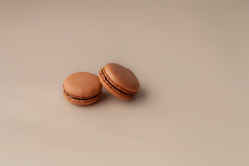 Two brown macaroons on beige background close up copy space