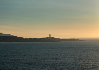Fototapeta premium Tower of Hercules on the horizon, illuminated by the last rays of sunlight at sunset. Located in A Coruña, Galicia, and of historical interest, copy space.