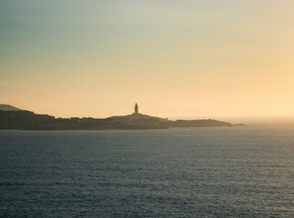 Tower of Hercules on the horizon, illuminated by the last rays of sunlight at sunset. Located in A Coruña, Galicia, and of historical interest, copy space.