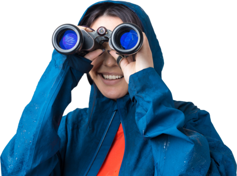 A tourist girl in a blue raincoat holds binoculars in her hands and looks into the distance, spies. - Powered by Adobe