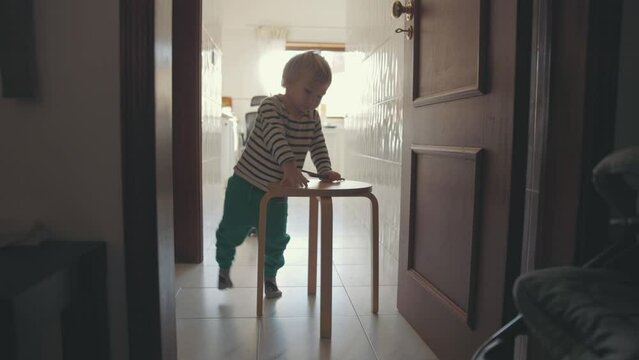 A little boy pushing forwards a chair holding colored pencils