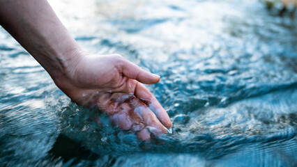 A female hand touching the river water - obrazy, fototapety, plakaty