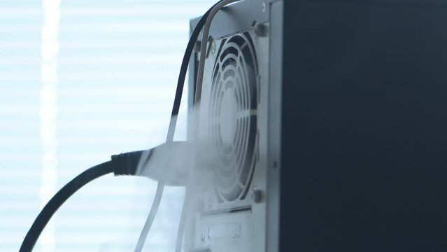 The computer system unit and the power supply are smoking. Concept: equipment overheating, heavy load, fire and ignition.