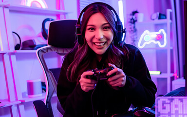 Beautiful happy young female game online streamer or caster smiling with fun, succeed for winner, using joinstick to play or compete, sitting in room with decorated neon light. Looking at camera.