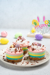 Fototapeta na wymiar Multicolored mini cheesecakes with candy eggs and whipped cream. Pastel colored Easter dessert