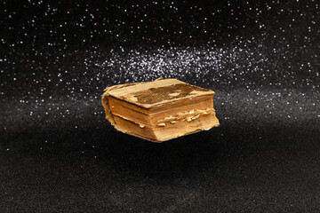 A tattered old vintage book levitating on sparkling black glittery background. Photo with selective focus and copy space