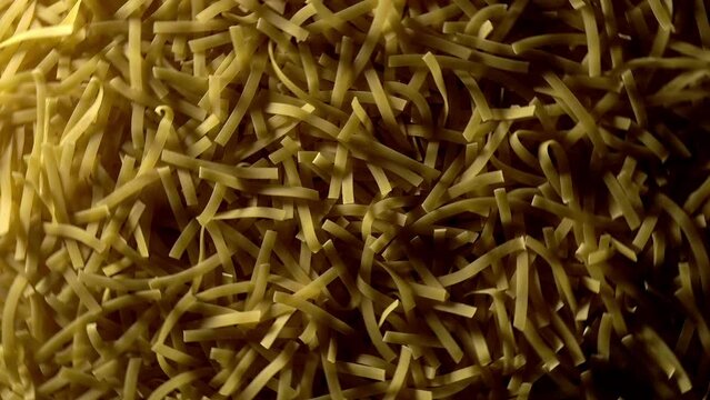 Uncooked Tagliatelle Lungo pasta rotating in fast motion - top view, flat lay, low key, food background. Raw dried organic golden long macaroni texture. Italian food, cuisine and culture close up