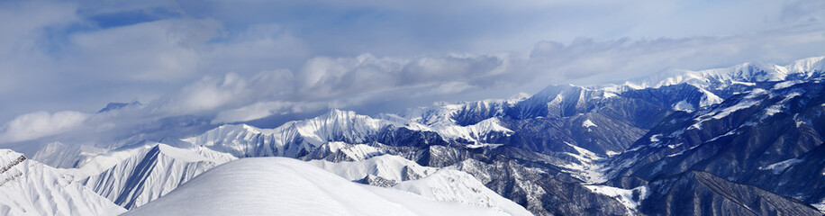 Panorama of off-piste snowy slope and cloudy mountains