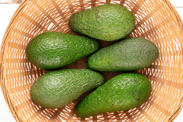 Several juicy avocados in a straw plate on a wooden table, macro, top view.