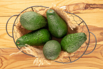 Several juicy avocados in a basket on a wooden table, macro, top view.