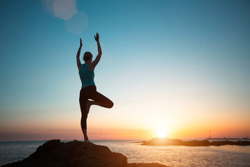 Yoga woman meditating on the rocks of the Atlantic during magical sunset.