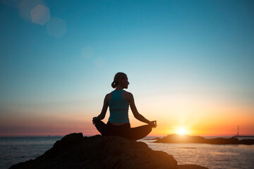 Silhouette of a middle-aged woman doing yoga on the ocean, during sunset.