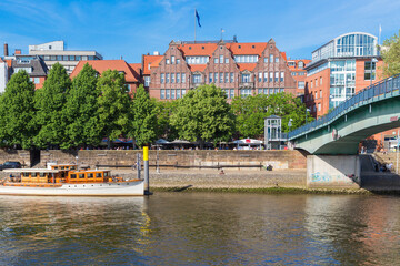 Obraz premium Cityscape of Bremen with old architecture, historical wooden sailing ships and barge floating along the river Weser. Bremen, Germany, July 15, 2021