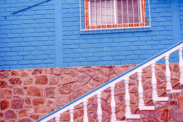 Abstract of stair banister in front of red stone wall and blue house with red window with bars in Mulege, Baja, Mexico