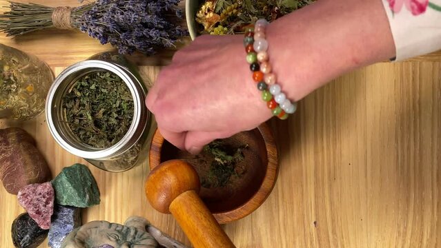 Table top view skilled female herbalist mixing various dried herbs with wooden mortar pestle indoors. Unrecognizable middle-aged woman using natural herbal methods of treatment. Alternative medicine
