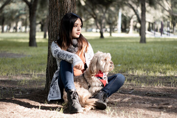 Girl and her dog. A girl is looking into the distance together with her dog in the park. A girl is sitting at the foot of a tree together with her dog in the park.