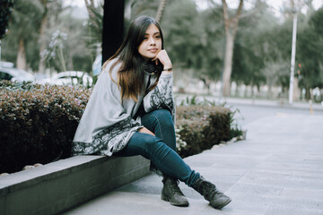 Girl looking into the distance pensive. Girl sitting alone in a city.