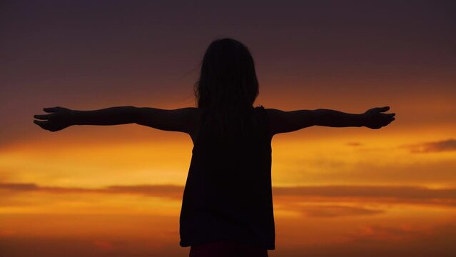 Silhouette of a girl with her arms raised to the sides against the backdrop of a beautiful sunset sky