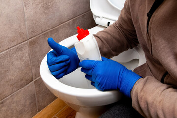 The cleaning lady near the toilet with cleaning agent shows the ok sign with her hand. The toilet is clean