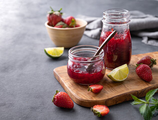 Two jars of strawberry jam on a wooden board on a dark background with fresh berries. Homemade sweets.