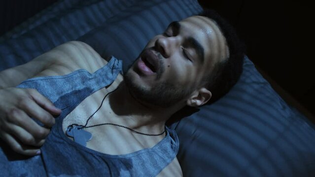 High angle view close-up of young Black military man lying on bed having panic attack after nightmare