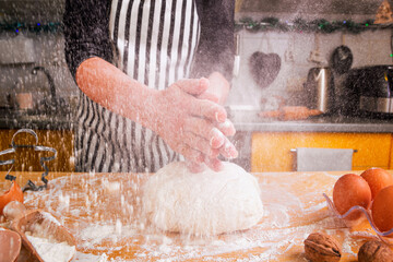 Pastry chef in a striped culinary apron sprinkles flour on the dough for homemade baking