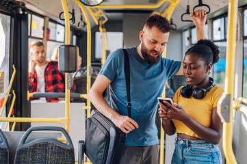 Multiracial friends talking and using a smartphone while riding a bus in the city - Powered by Adobe
