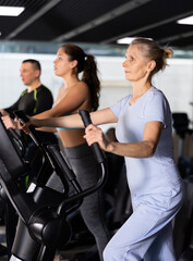 Fototapeta na wymiar Mature female athlete working out at elliptical machine in gym