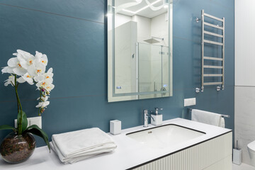 Blue and white bathroom with big mirror, towels, lighting and countertop basin.