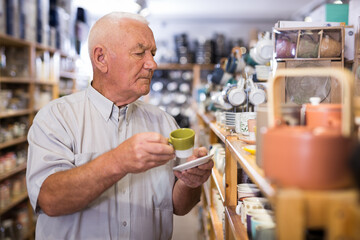 Elderly male customer chooses plates and cups in tableware store