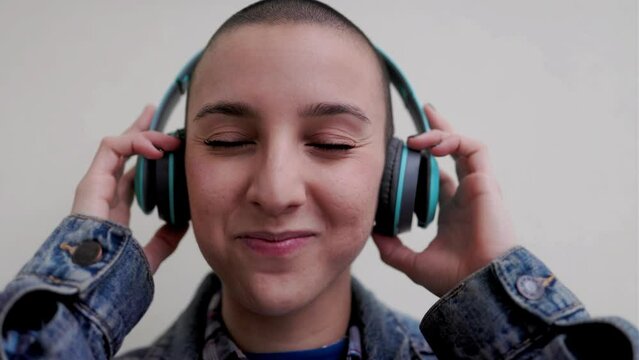 Happy bold young woman listen playlist music with headphones outdoors - Diversity androgynous joyful concept