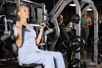 Fototapeta na wymiar Portrait of elderly woman during workout with power exercise machine in gym club