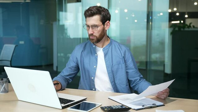 Mature businessman in shirt doing paperwork man working with documents contracts and bills sitting at table using laptop at work, financier accountant bookkeeper with beard and glasses entrepreneur