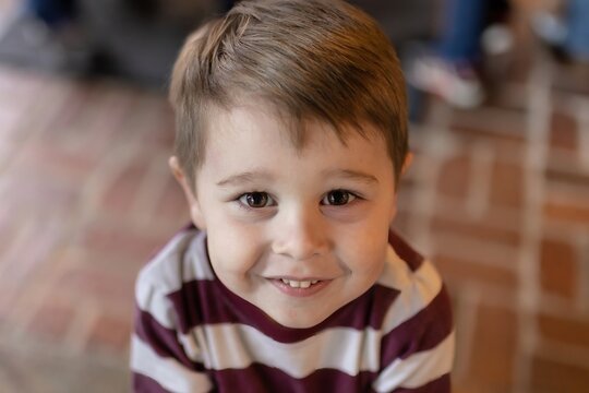 portrait of a cute little boy close up smiling with front teeth showing and brown eyes looking up with bokeh in background, horizontal
