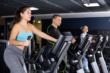 Sporty young woman using elliptical machine in gym