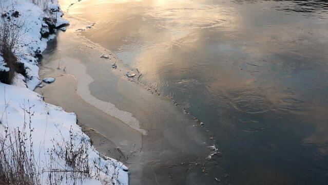 Sun shine on water on winter cold river covered in snow. Water flow at sunset, static footage