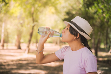 woman drinking bottle of water in forest
