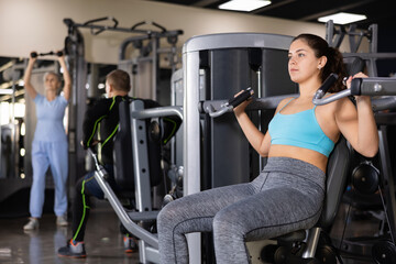 Fototapeta na wymiar Active young woman training at overhead press machine in gym