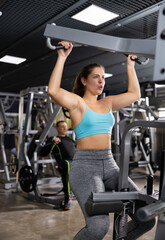 Fototapeta na wymiar Active young woman training at shoulder press machine in gym
