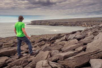 Male tourist in green shirt standing on edge of a cliff. Aran Island, Ireland. Travel and tourism....